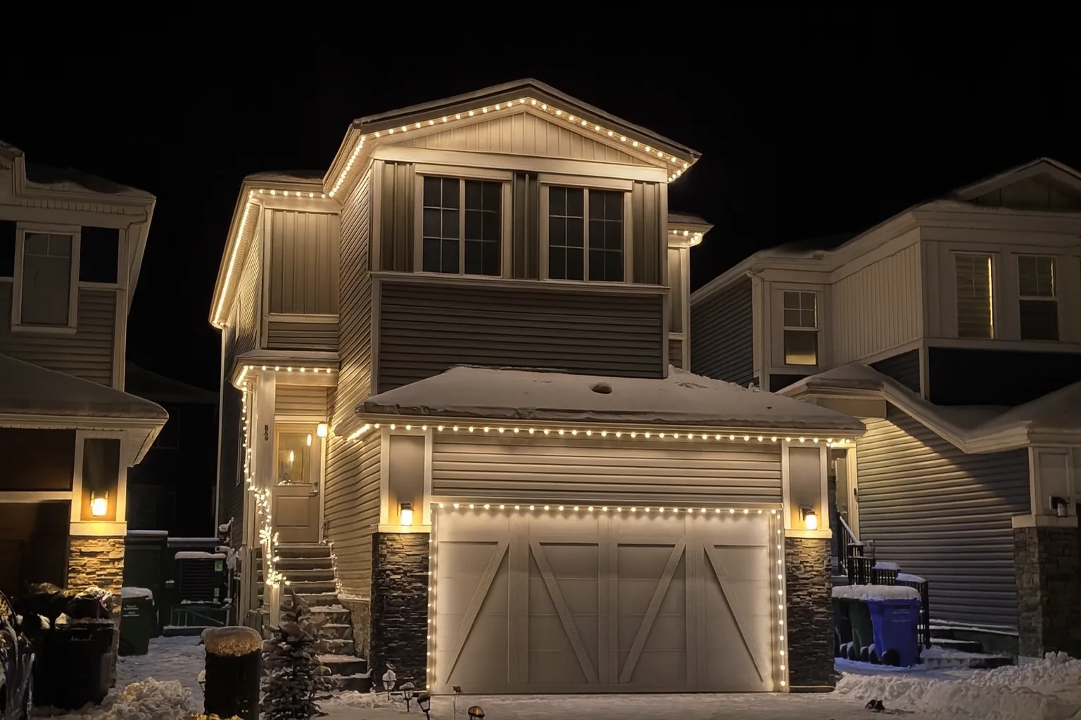 Warm-white permanent Christmas lights outlining a snow-covered Kelowna home