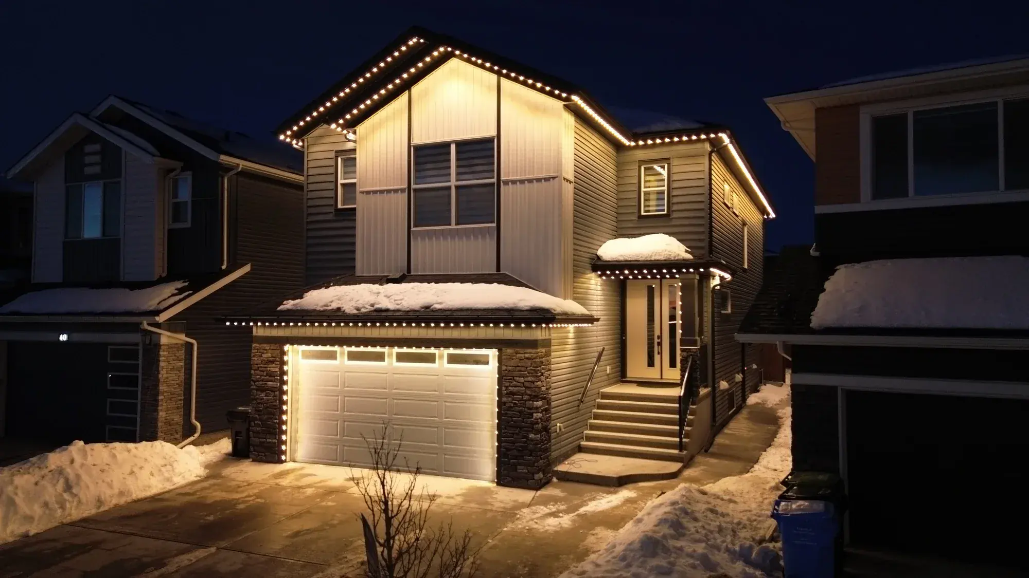 Edmonton home with warm-white permanent lights outlining its roofline in winter